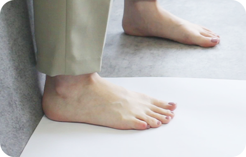 壁に沿って置いた紙に足をのせる様子
